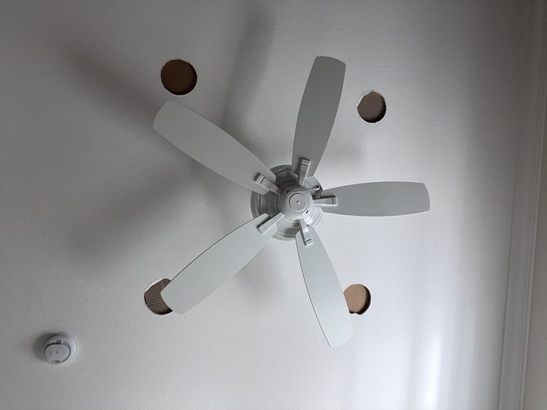 Smooth white ceiling with four rectangular openings cut around a ceiling fan, ready for drywall repair