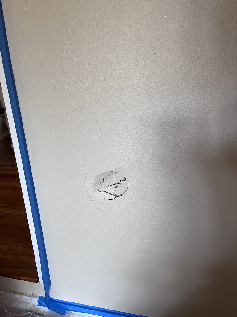 Joint compound being applied over a drywall patch with the adjacent trim masked